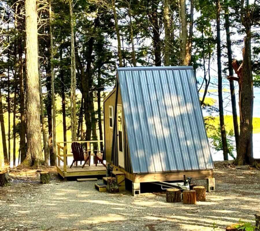 A-Frame tiny house with metal roof on wooden foundation in wooded area.
