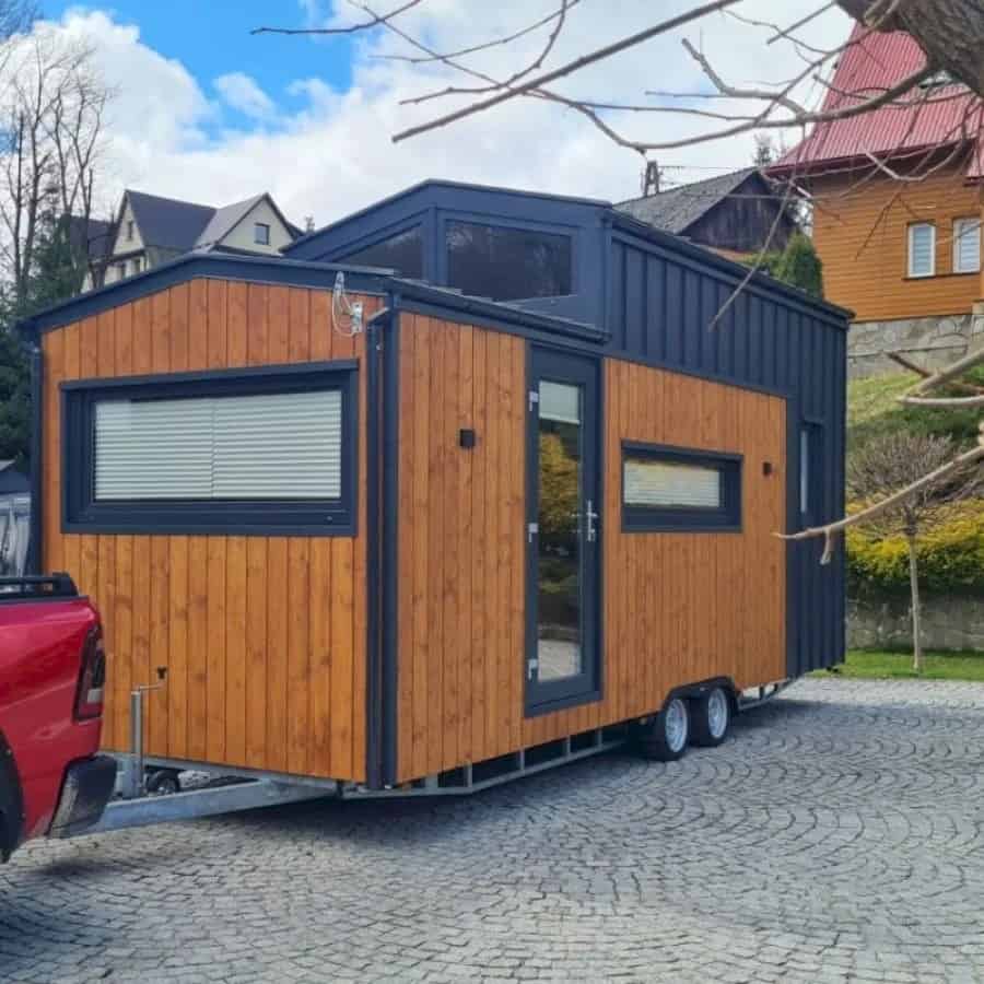 The Adams tiny house by Craft House with honey-toned wood siding and a charcoal metal gable, on its trailer