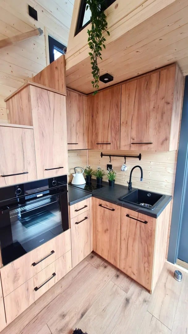 Real-wood kitchen in the Adams tiny house with a black oven, induction hob, and a black sink