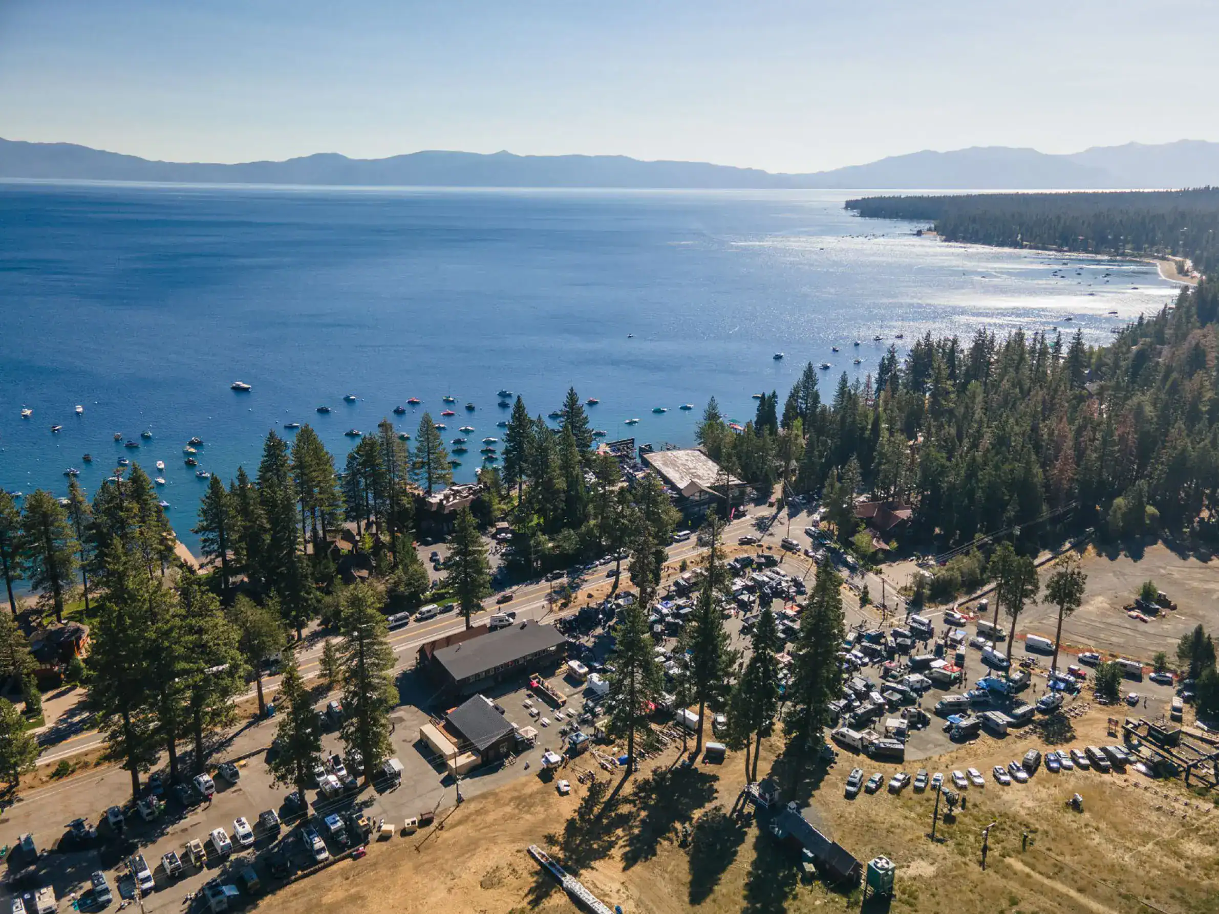 Aerial view of the Adventure Van Expo with vans parked along the shore of Lake Tahoe surrounded by pines