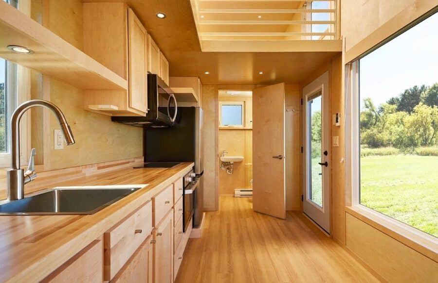 Compact tiny house interior with modern kitchen and large windows.