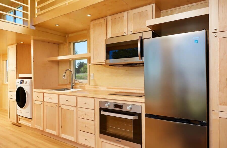 Compact tiny house kitchen with modern appliances and natural wood finishes.