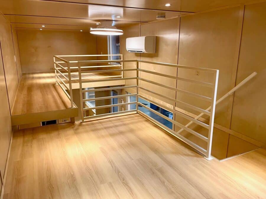 Interior view of a tiny house on wheels featuring a safety railing and wooden finishes.