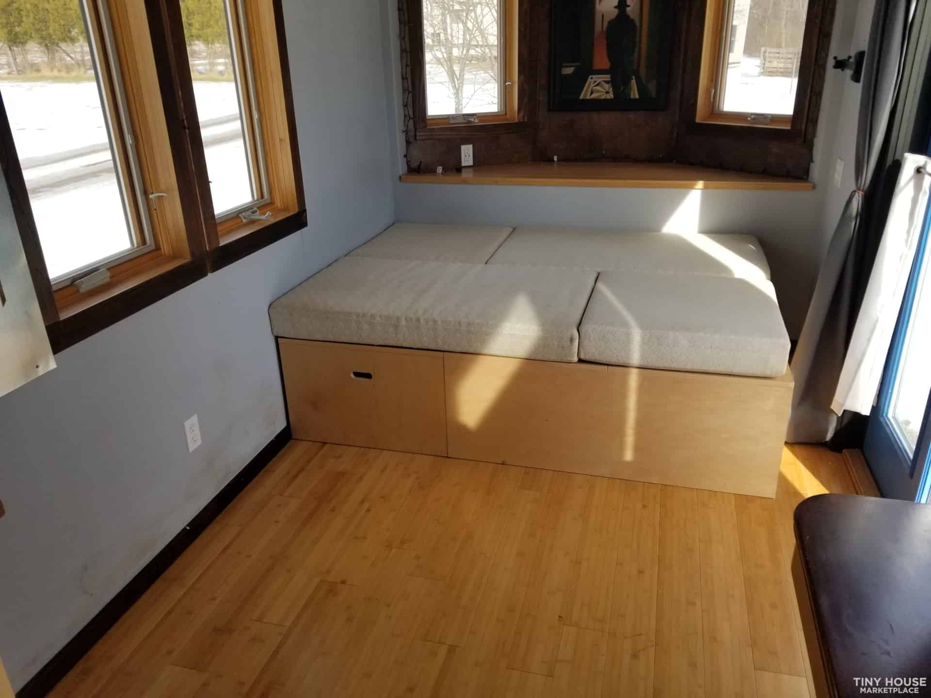 Compact tiny house interior with a built-in daybed near windows.