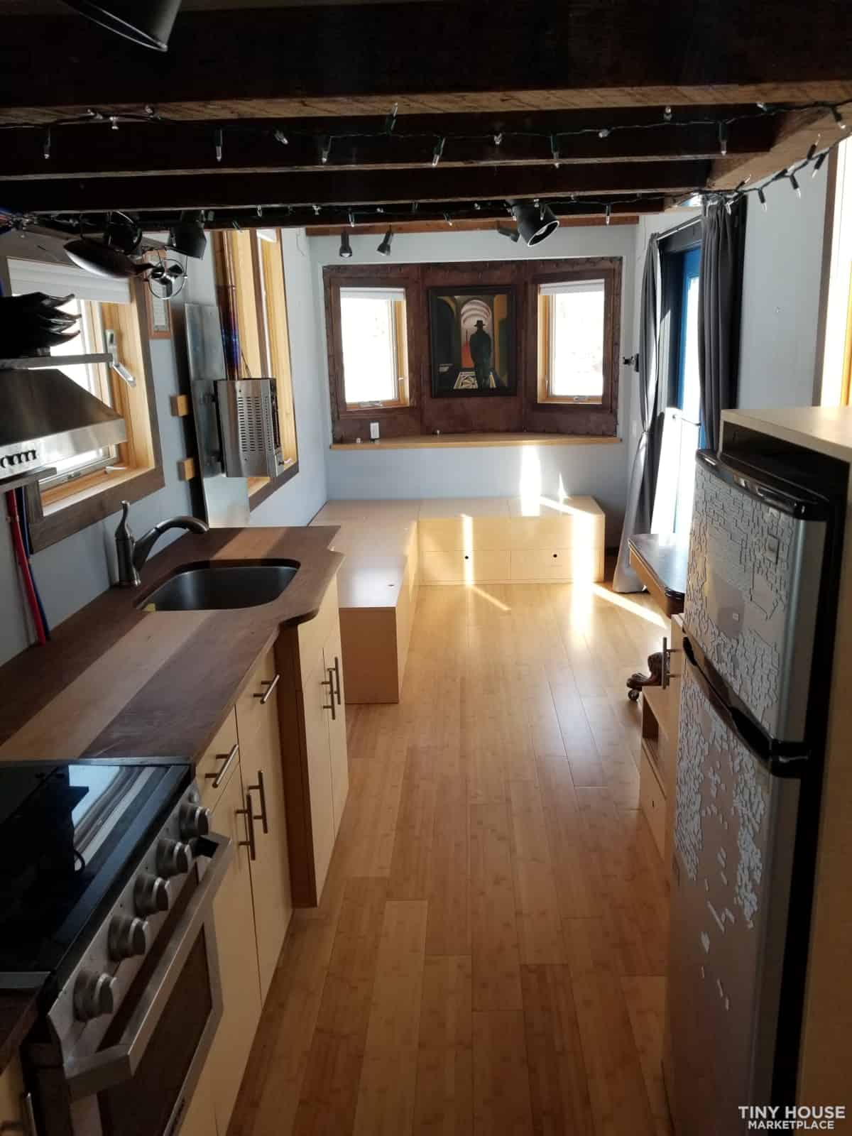 Compact tiny house kitchen with wooden accents and large windows.