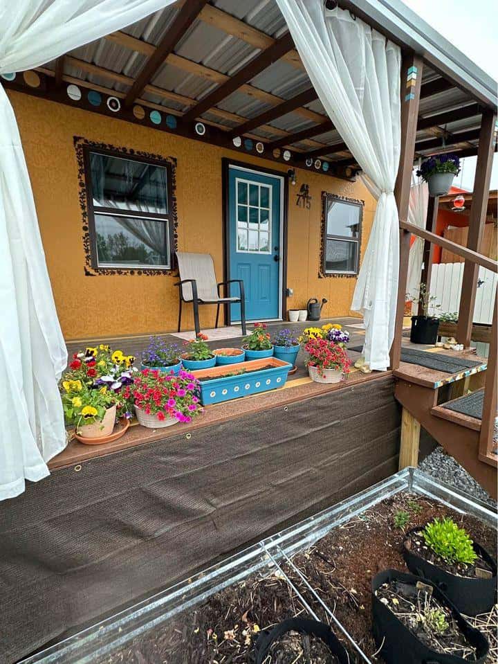 Cozy tiny house with vibrant porch, potted plants, and garden beds for small space living.