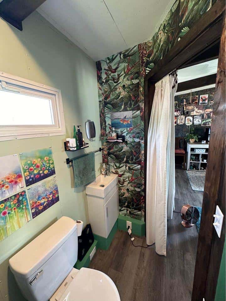 Compact tiny house bathroom with a toilet, sink, and colorful wall decor.