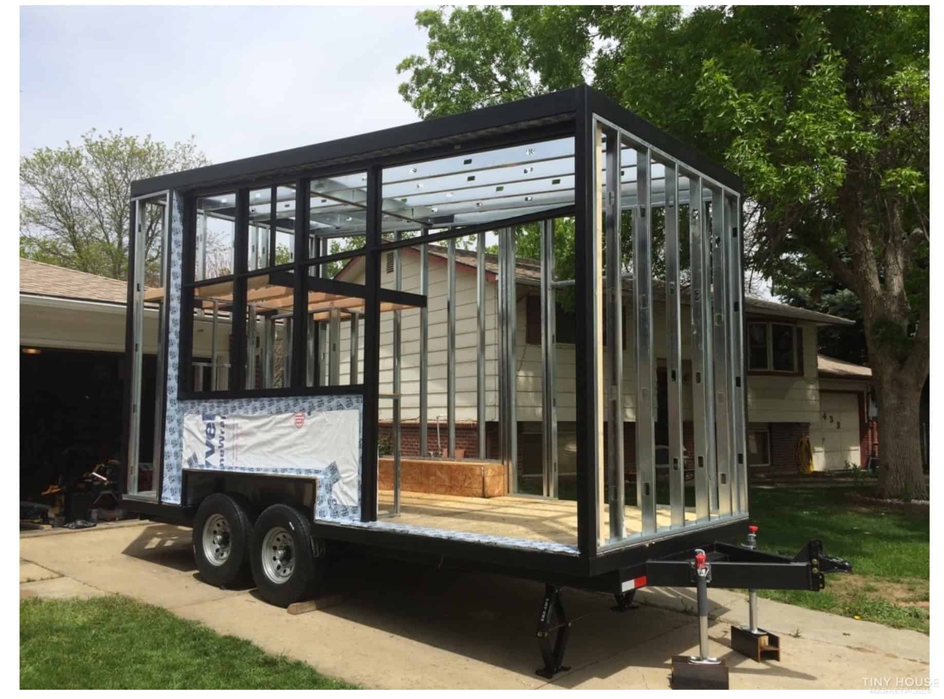 Mobile tiny house with glass walls on trailer for flexible living options.