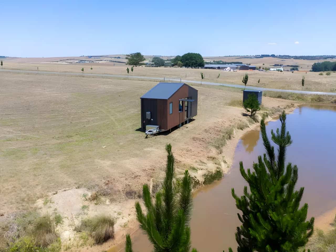 Aerial view of the Audrey tiny house sited on open grassland beside a dam, showing how the compact 7.2-meter home fits a rural block