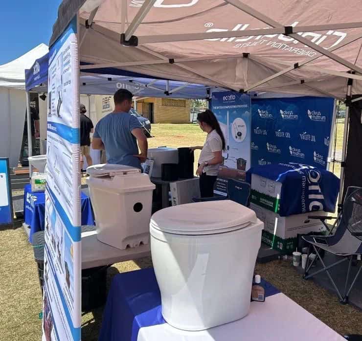Composting toilet exhibitor stand with multiple units on display at an outdoor tiny home expo