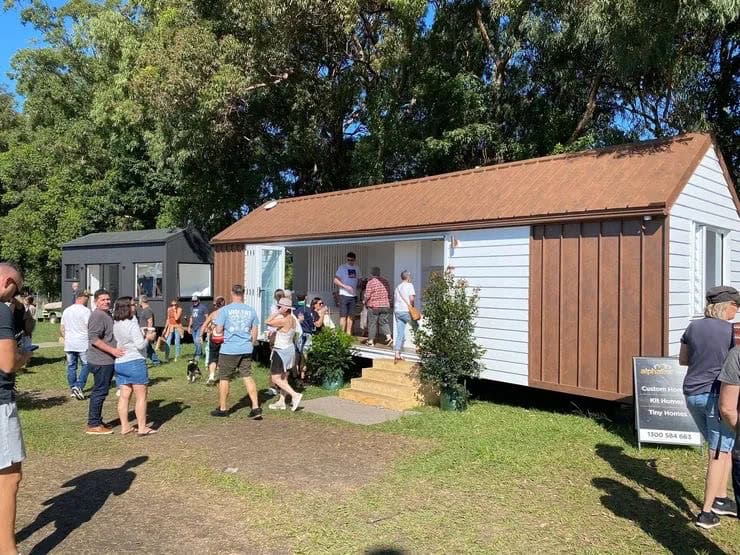 Visitors walking between tiny homes displayed on grass at an Australian Tiny Home Expo