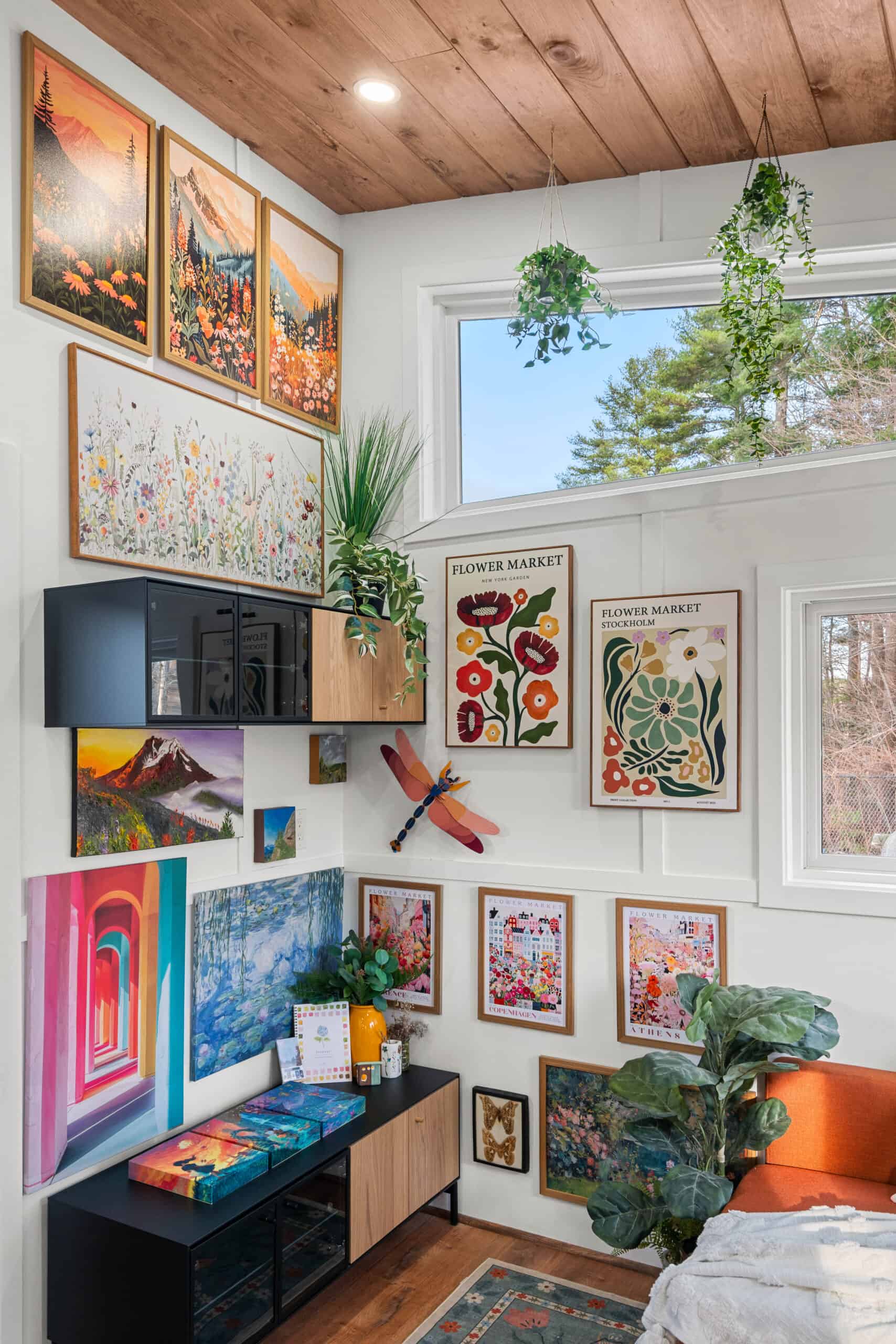 A colorful gallery wall of framed art climbing toward the clerestory windows inside The Knoll