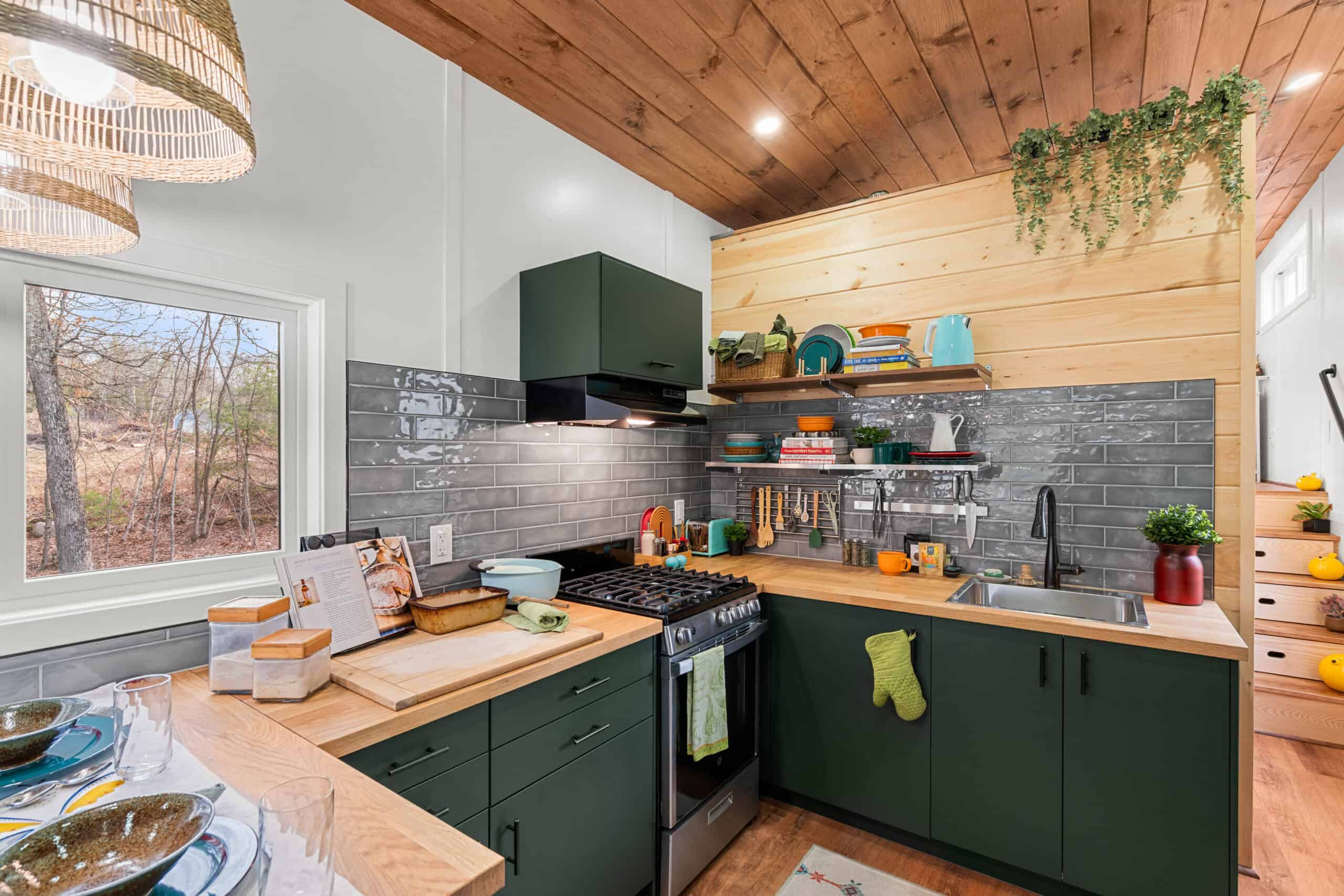 The Knoll's kitchen with deep green cabinets, a wood countertop, gas range, subway tile, and open shelving