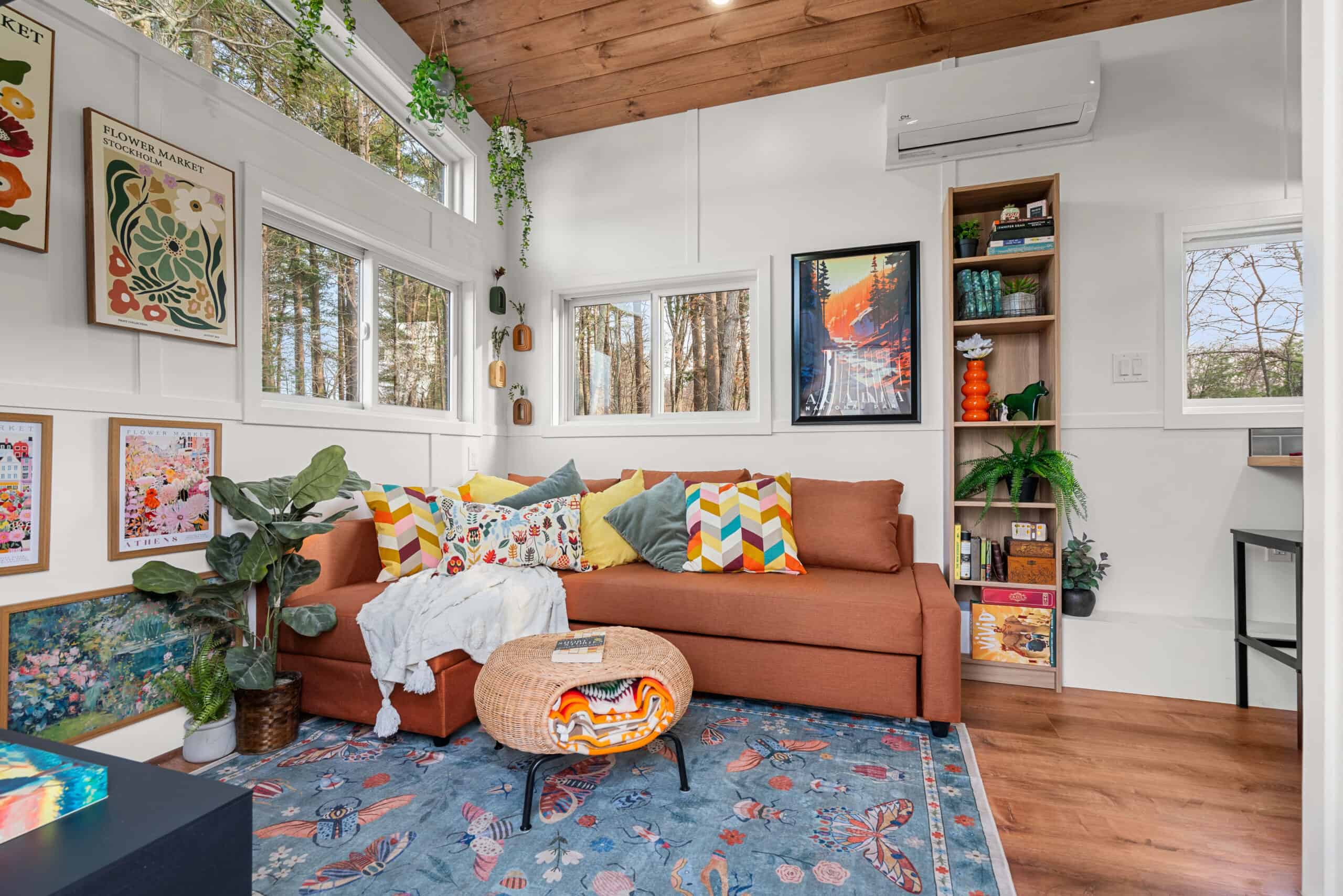The Knoll's living room with a burnt-orange sleeper sofa, bookshelves, a mini-split, and walls of windows