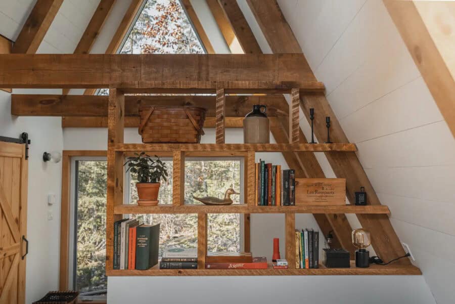 Charming A-Frame bedroom with wooden shelves and natural light, perfect for a small space getaway.