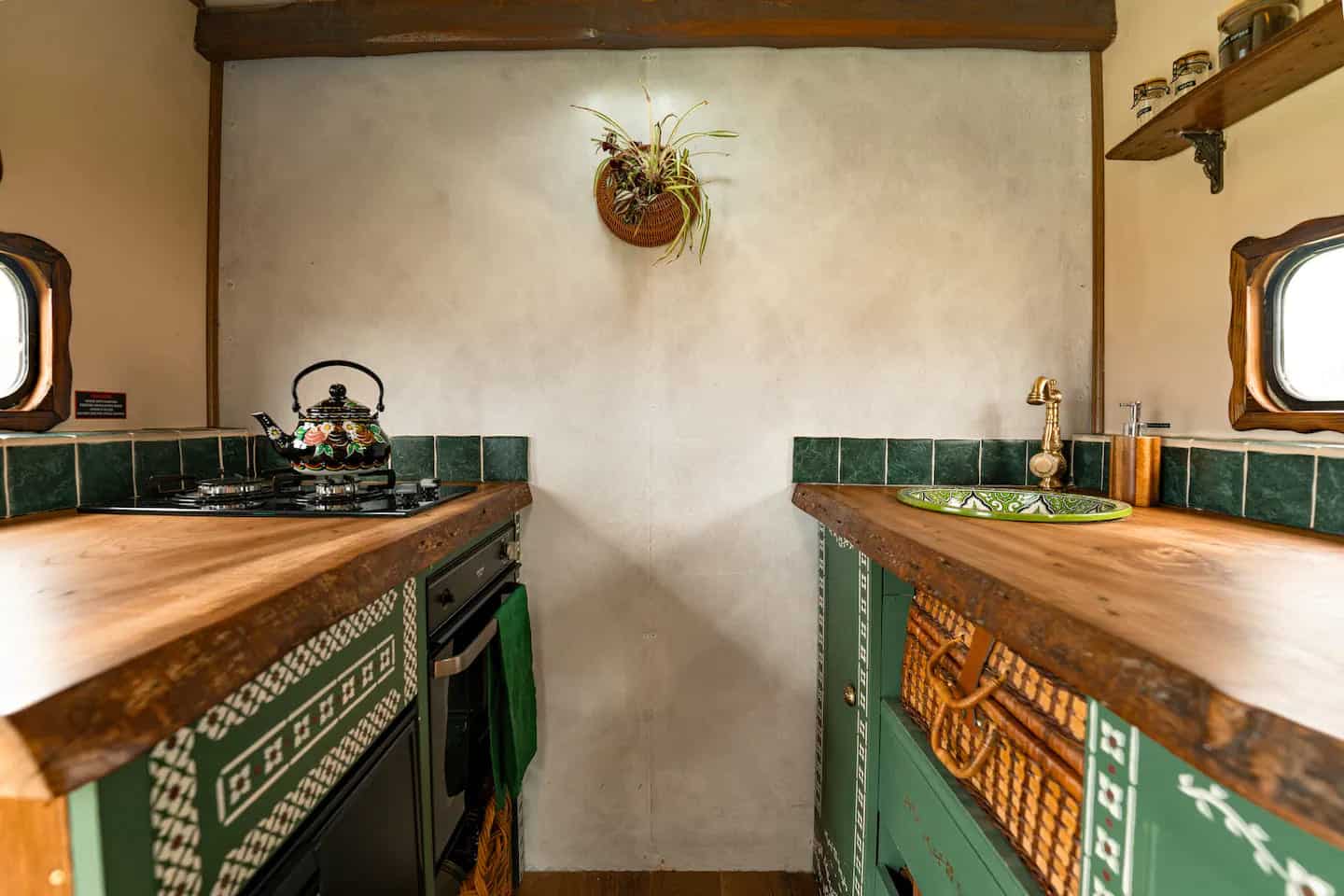 Galley van kitchen with green stenciled cabinets, reclaimed elm worktops, gas hob, and a Moroccan brass sink