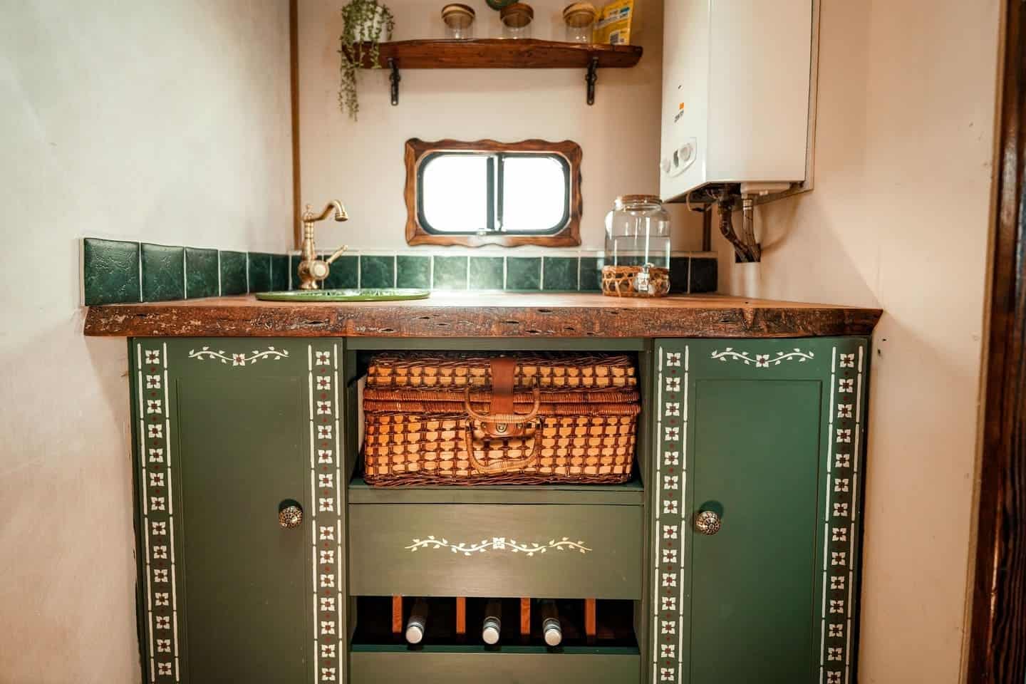 Close-up of the green stenciled van kitchen cabinet with a wicker picnic hamper and wine rack storage