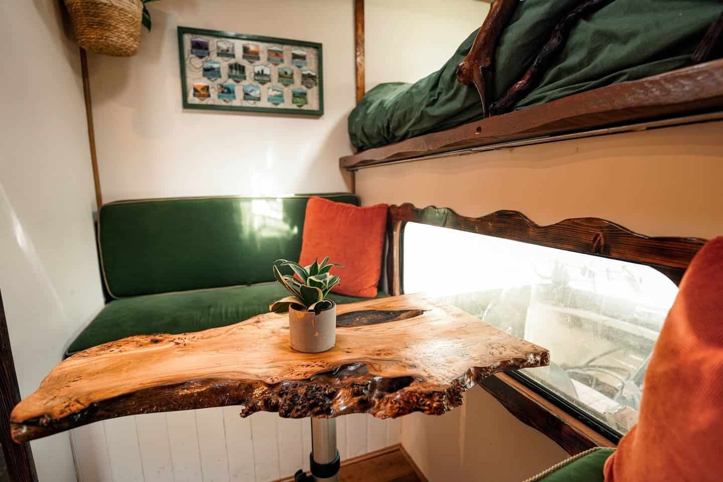 Live-edge elm dining table with green velvet bench seating and a carved wooden window frame in the van