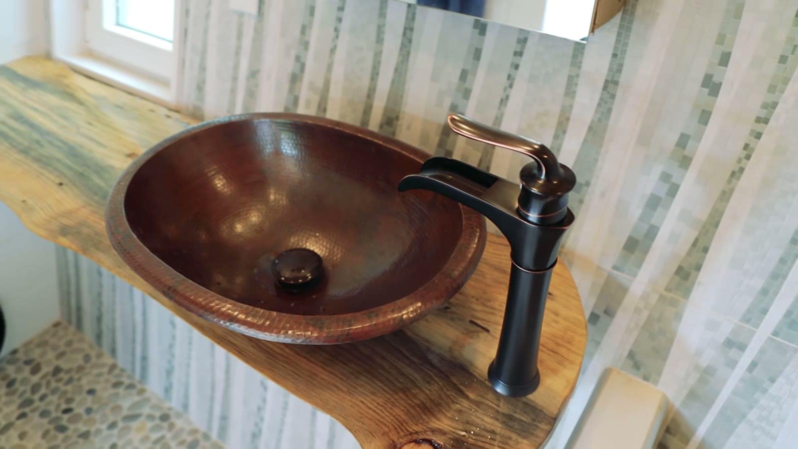 Hammered copper vessel sink with an oil-rubbed bronze faucet on a reclaimed wood counter