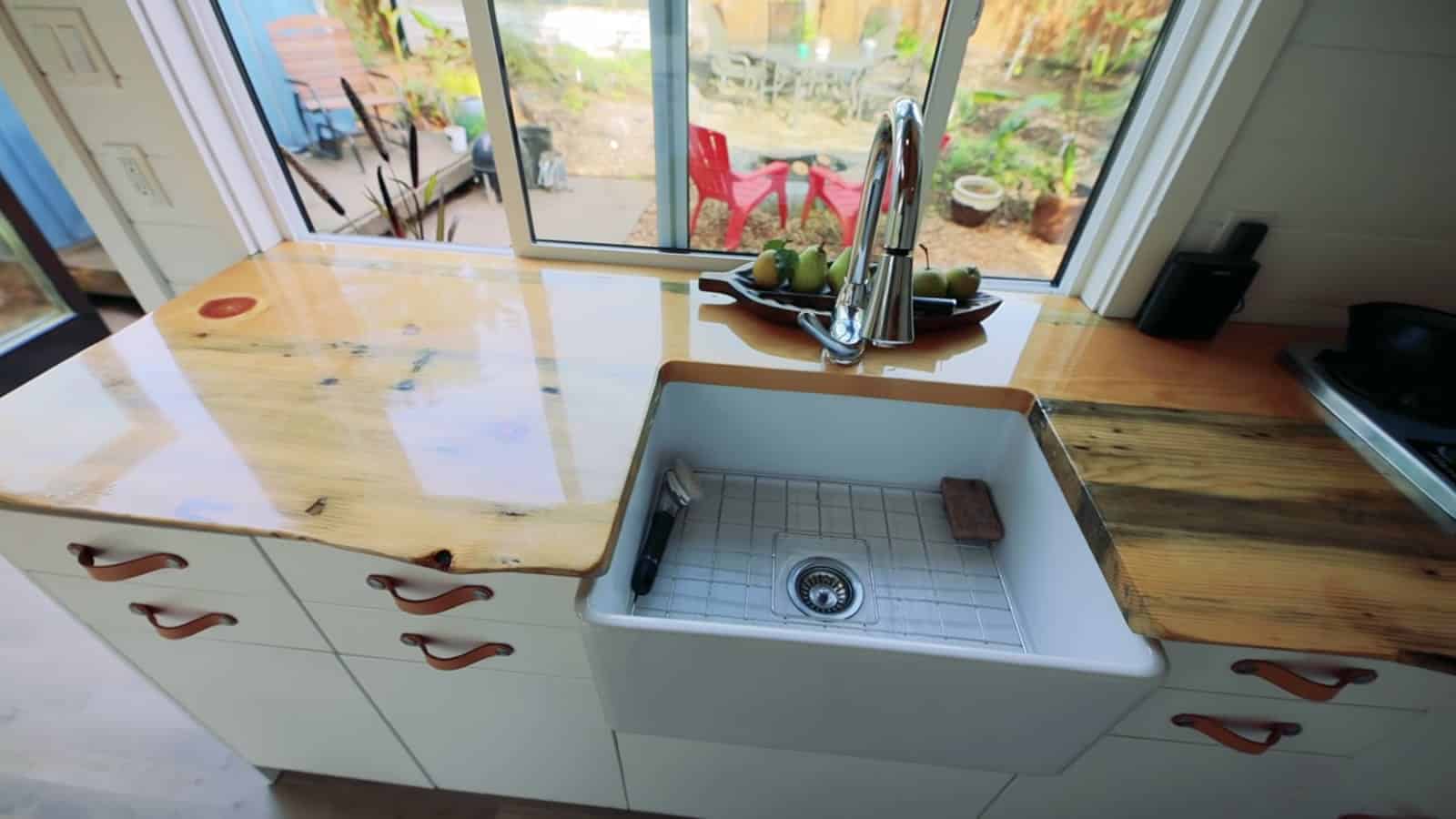 Deep white farmhouse sink set into the beetle-kill pine counter under a garden window