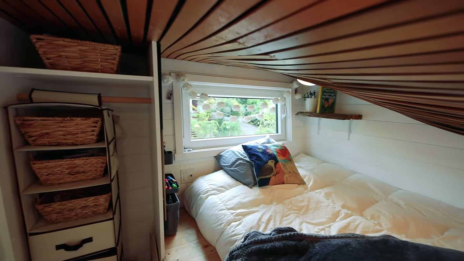 Kid's sleeping loft over the living room with futon, window and wicker basket storage