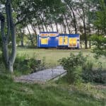 Scandinavian tiny house with office setup in a lush green outdoor setting.