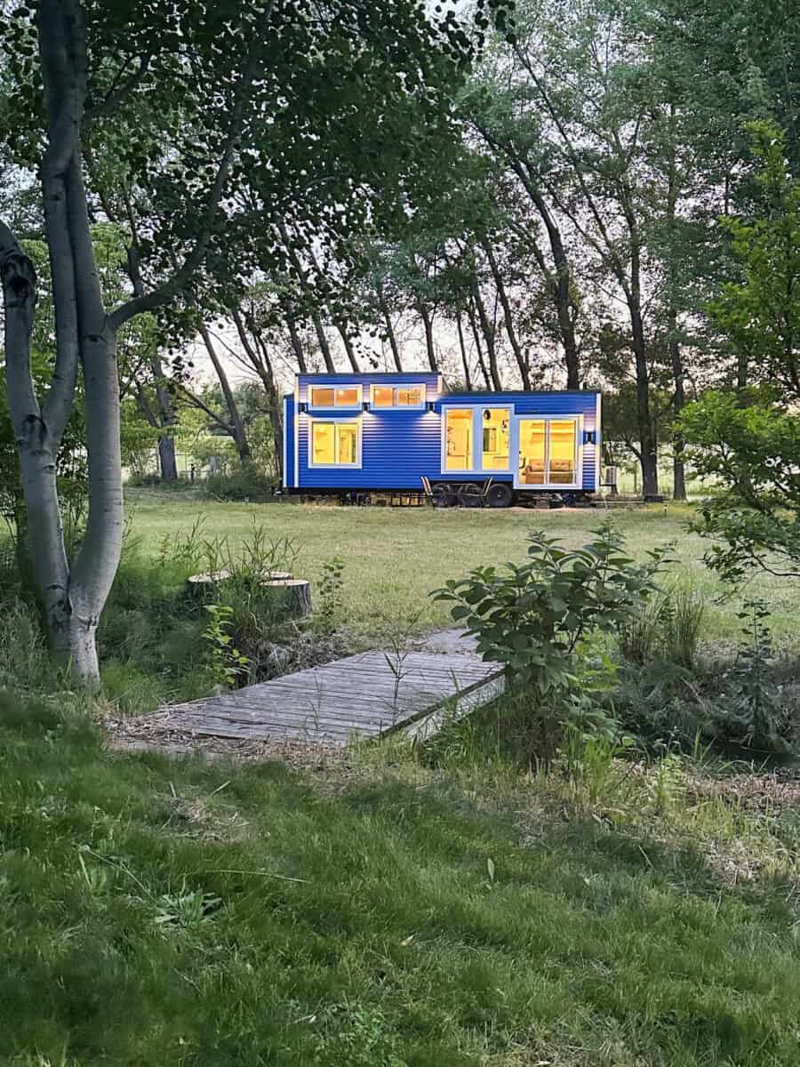 Scandinavian tiny house with office setup in a lush green outdoor setting.
