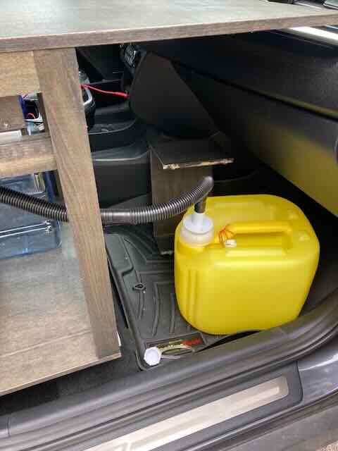 Stealth camper interior showing a yellow water container and compact storage under the dashboard.