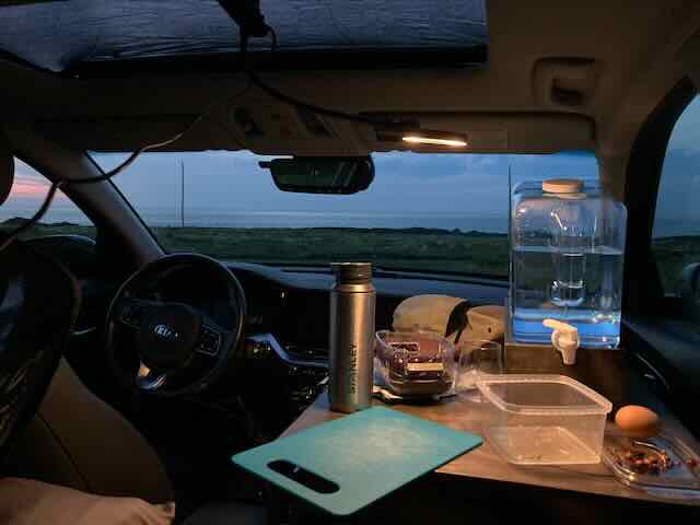 An inside view of Blake's Kia Niro EV stealth camper car showing essentials like water, snacks, and.
