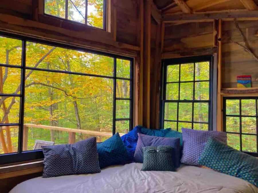 Treehouse interior with large windows overlooking colorful autumn trees.