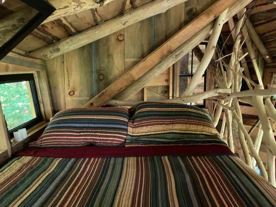 Charming treehouse bedroom featuring rustic wooden walls and colorful striped bedding, offering a pe.