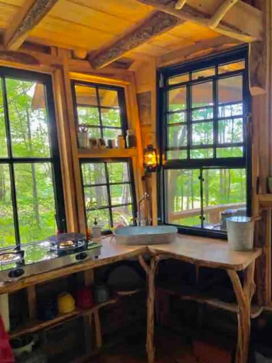 Compact tiny house kitchen featuring large windows and rustic wooden accents.