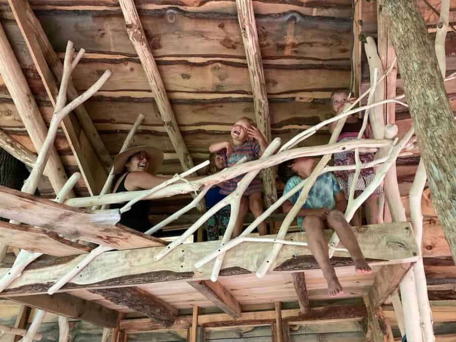 Elevated treehouse interior with children playing on natural wood branches and rustic wooden walls.