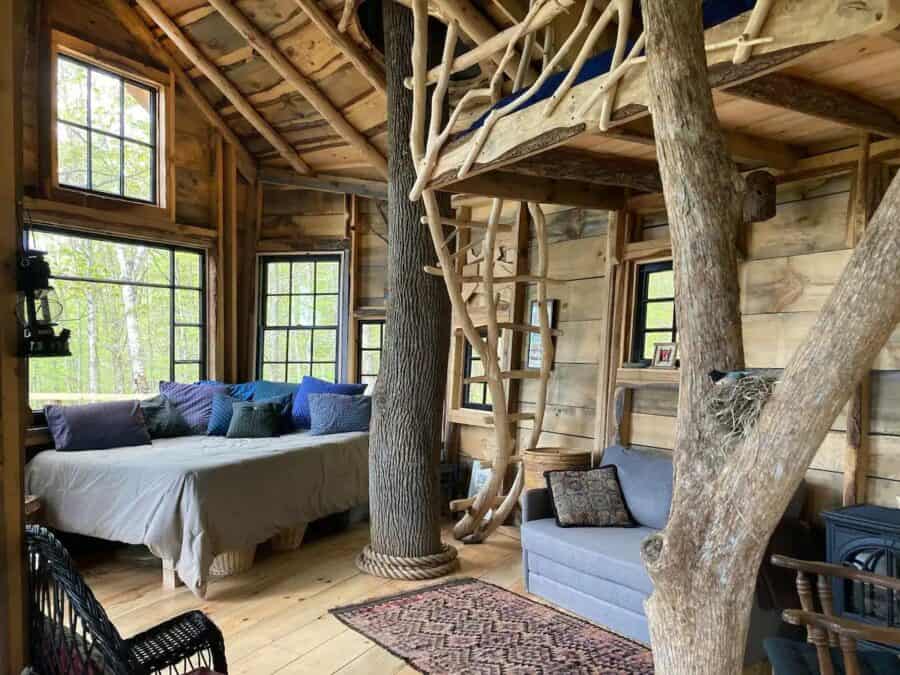 Charming treehouse living space featuring natural wood finishes and large windows with mountain scen.