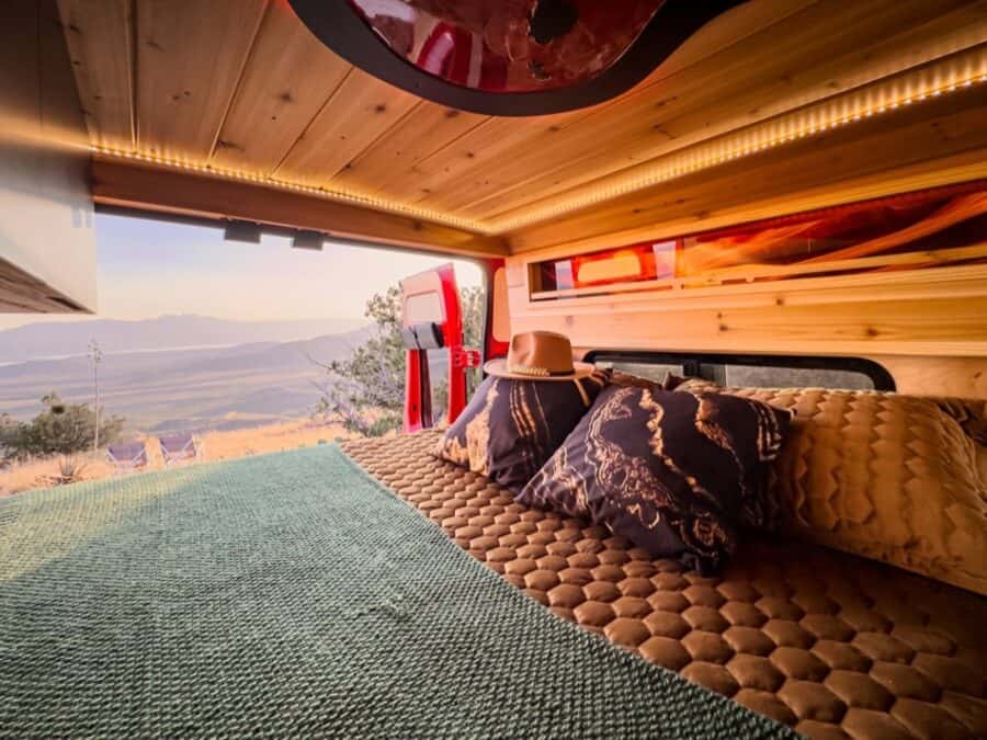 Interior of a boho-style camper van with a view of mountains and sunset.