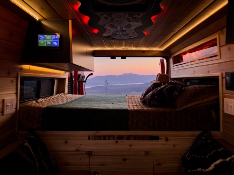 Interior of a modern camper van with a large bed and scenic mountain view through the window.
