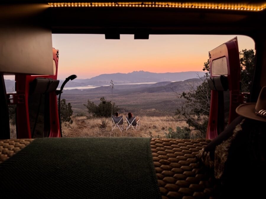 Compact camper van interior with panoramic view of mountains at sunset.