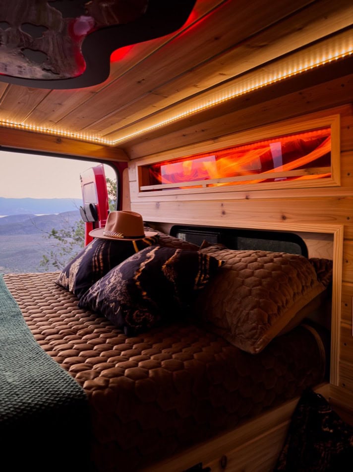 Charming boho-style camper van bedroom with warm wood accents and ambient lighting.