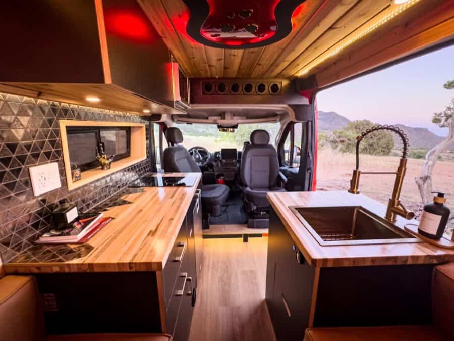 Interior of a boho-style camper van with wooden accents and scenic mountain view outside.