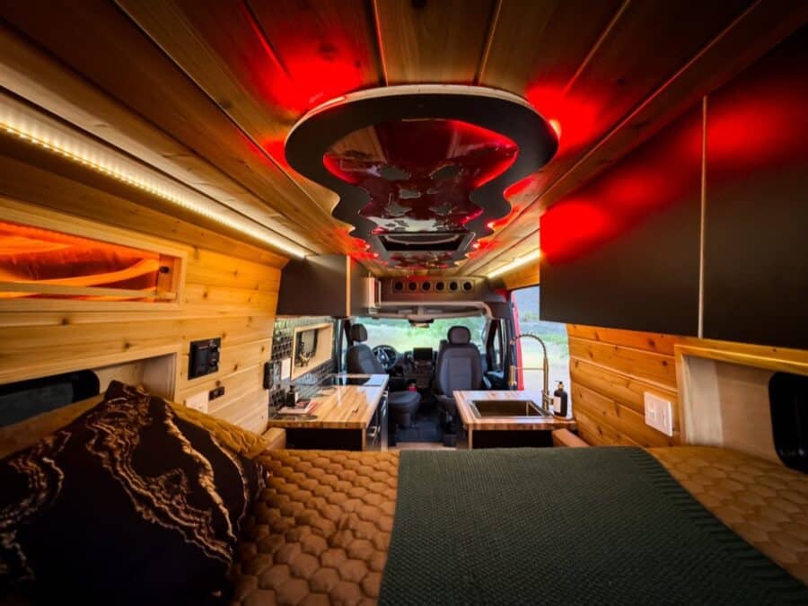 Compact boho-style camper van with warm wood accents and ambient red lighting.