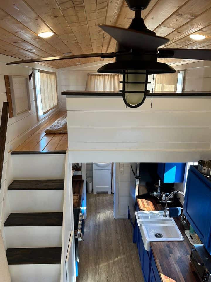 Interior view of a tiny house with a double loft, blue kitchen cabinets, and wooden accents.