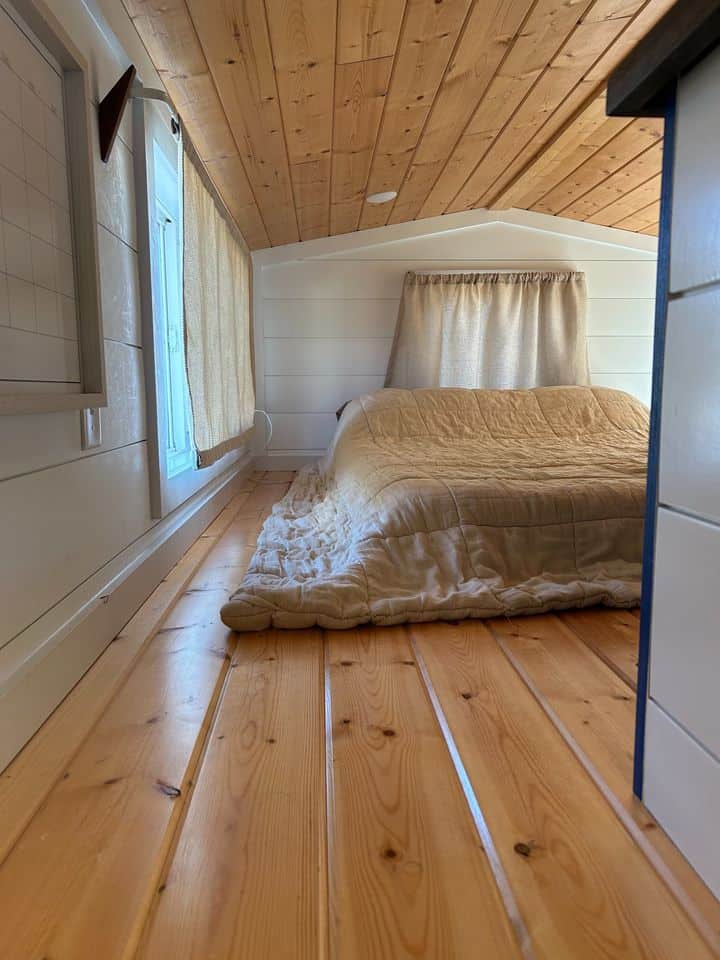 Double loft tiny house with wooden ceiling and cozy bed setup.