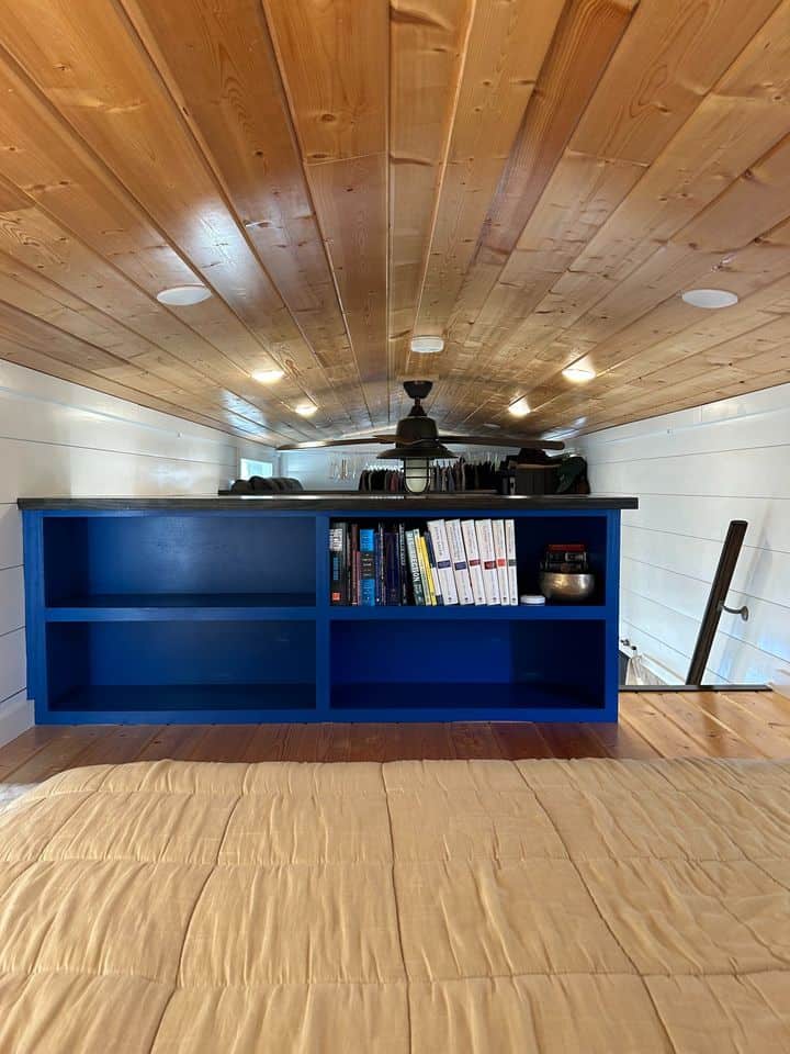 Blue double loft in tiny house with wooden ceiling and bookshelves.