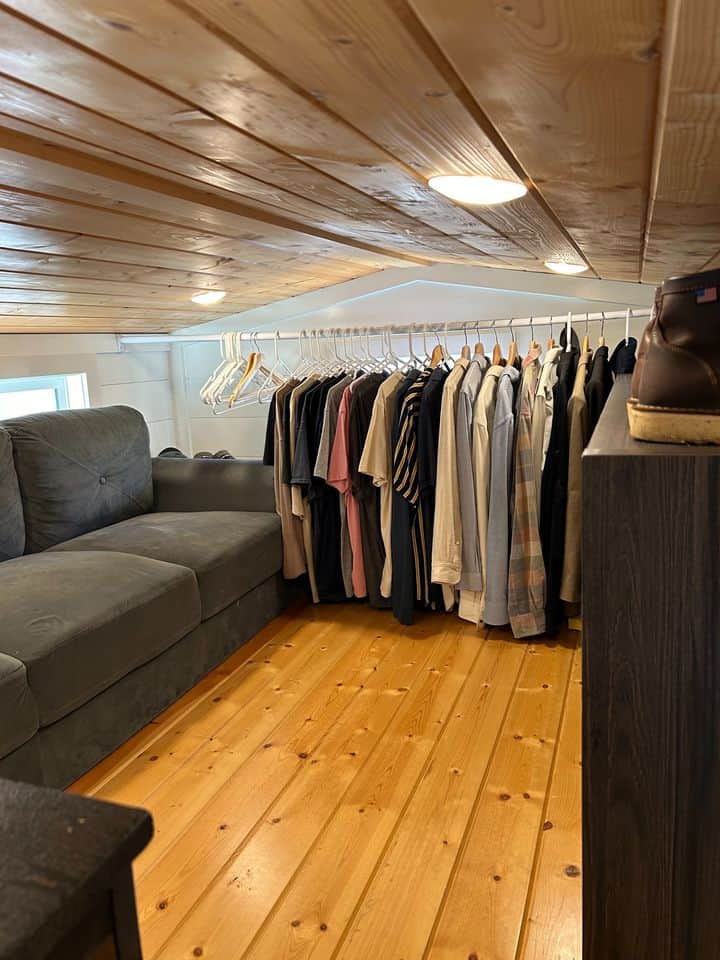 Small loft closet with hanging clothes and a gray sofa in a tiny house.