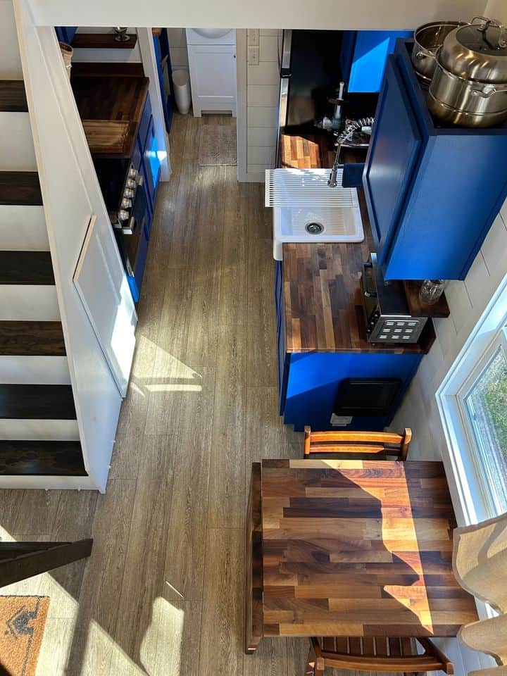 Blue double loft tiny house kitchen with compact appliances and wooden accents.