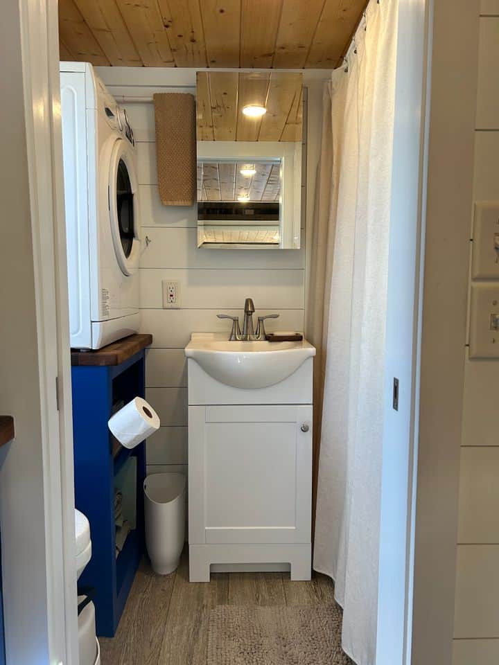 Blue and white tiny house bathroom with laundry area and small sink.