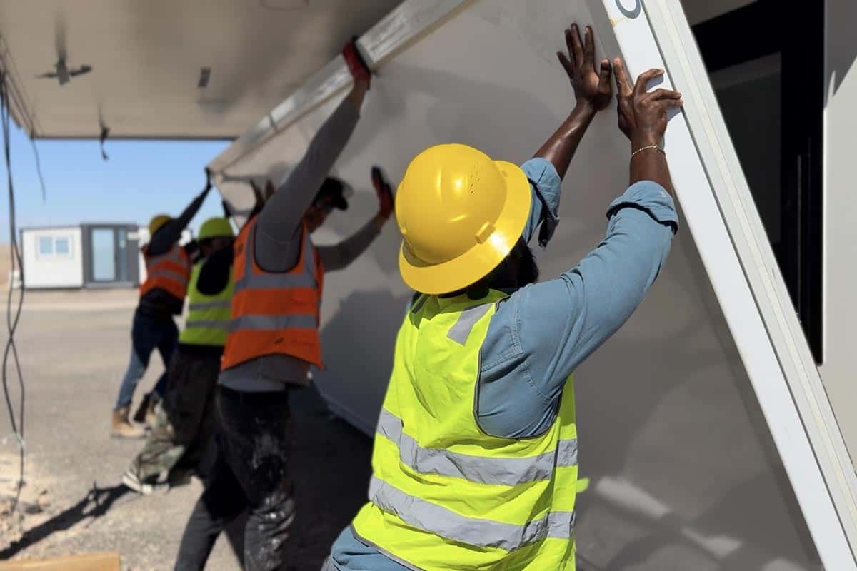 BoxHouse crew in hard hats raising a hinged wall panel into position during a site deployment