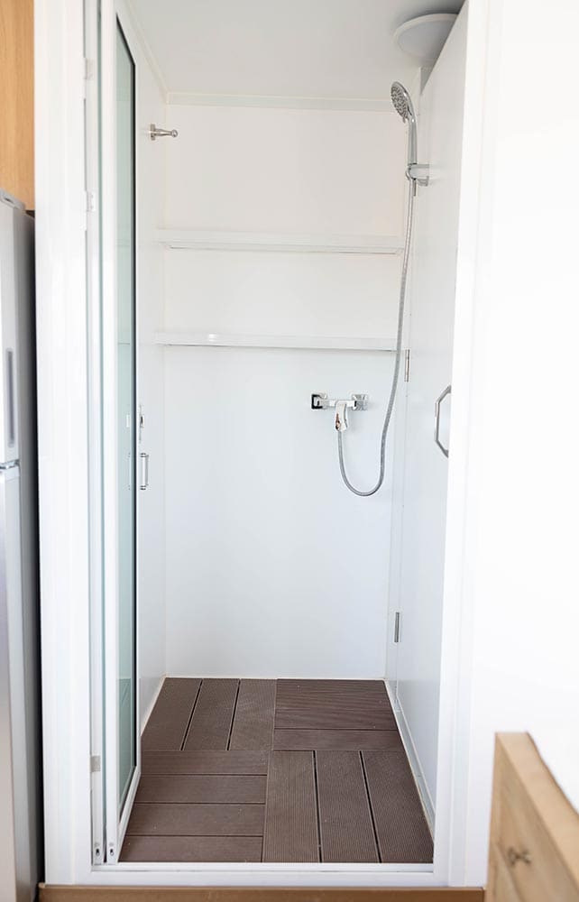 BoxHouse bathroom shower with glass door, built-in shelving, and composite deck-style floor tiles