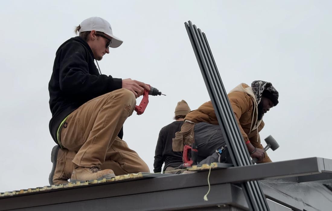 BoxHouse crew members installing standing seam metal roofing panels on top of a deployed unit