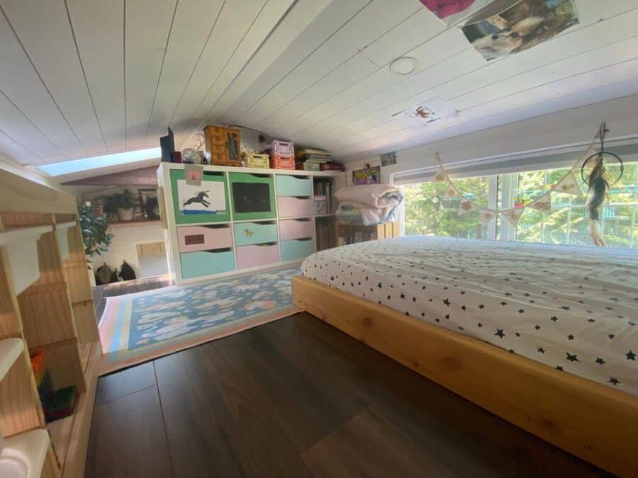 Compact tiny house bedroom with built-in storage and large window views.